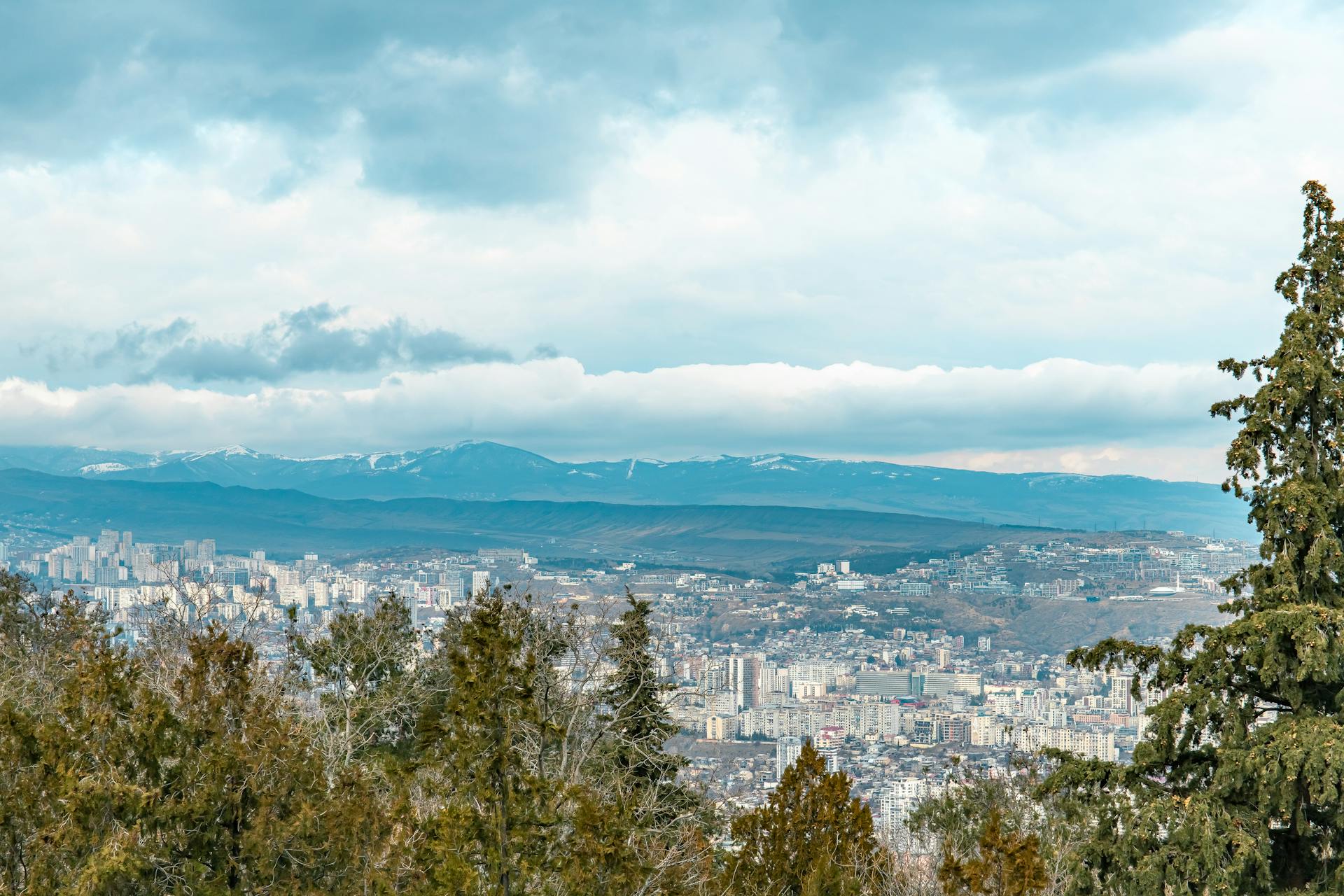 Aerial view of Tbilisi and surrounding mountains with cloudy skies.