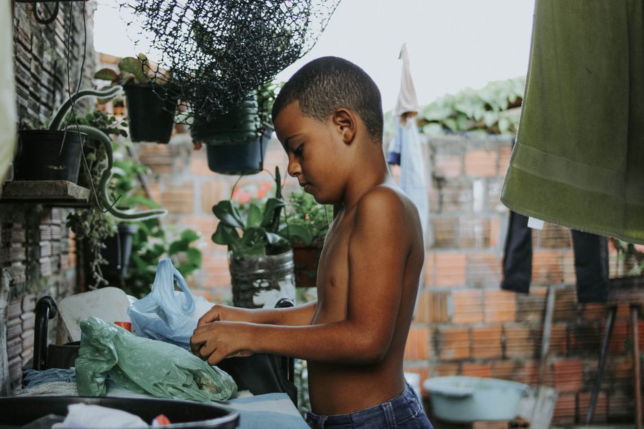Photo by Gabriel Frank on Pexels Un niño se encuentra en un patio rural, organizando artículos sobre una mesa rodeada de plantas. - Foto de Gabriel Frank en Pexels