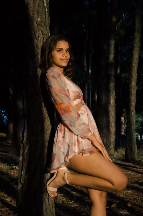 Free A woman in a floral dress leans against a tree in a forest setting. Stock Photo