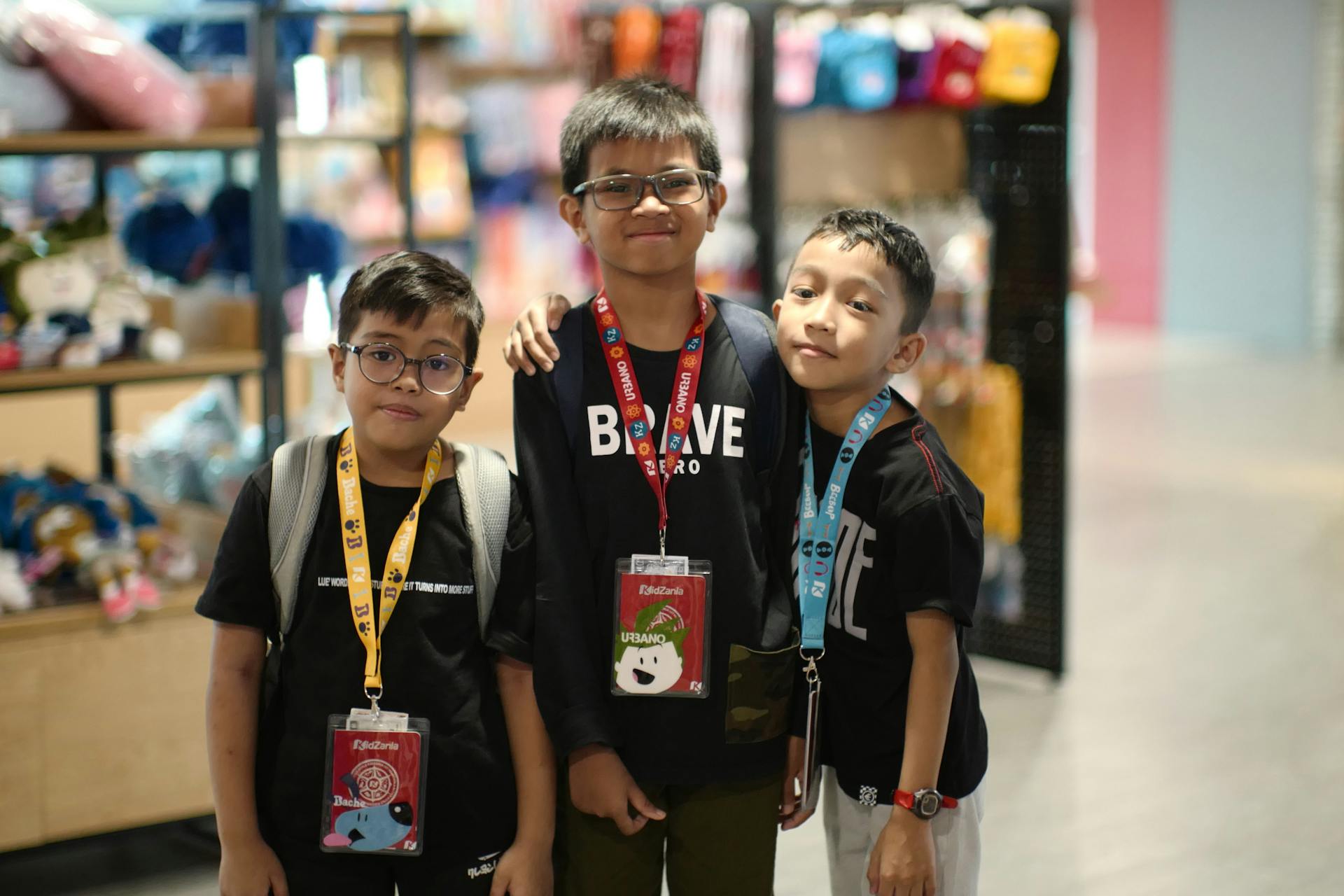 Three children standing together in a store, wearing ID badges and smiling.