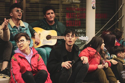 Men and Women Sitting in Town and Playing Guitar