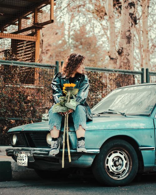 Free Woman in jeans with sunflowers sits on a vintage car outdoors. Stock Photo