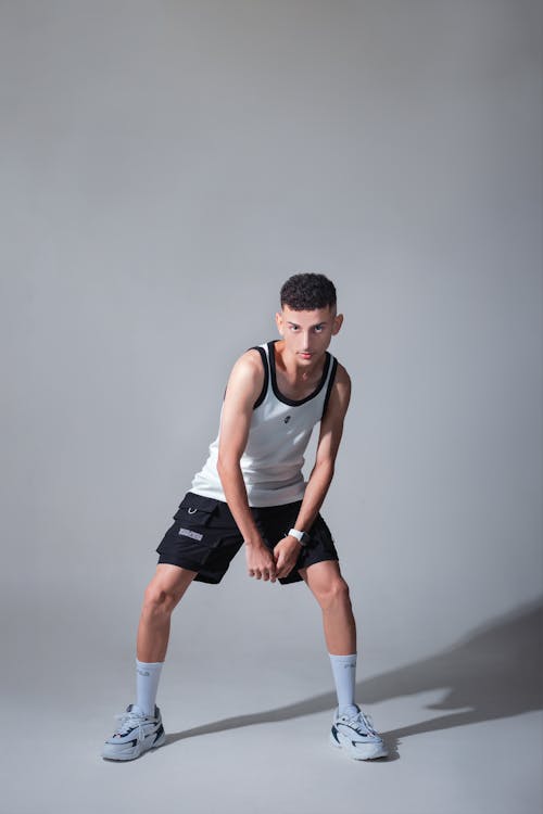 A young man in black shorts and white tank top posing