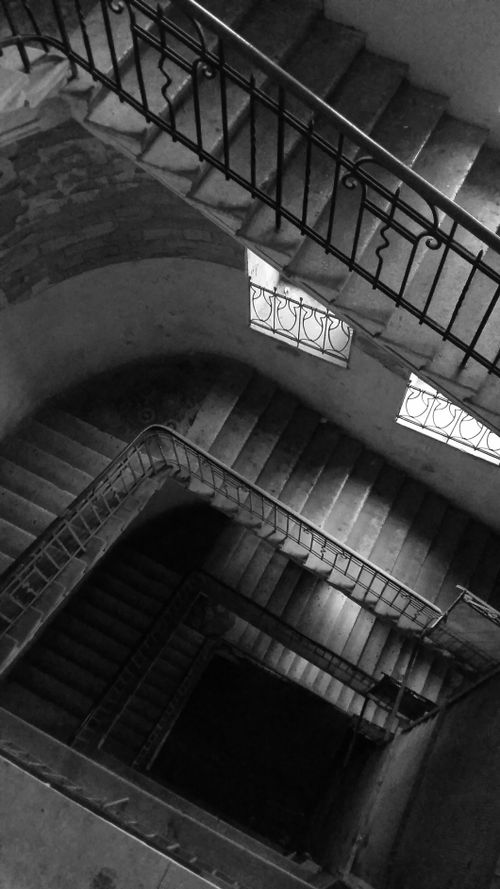 Free Black and white image of a spiral staircase with ornate railings captured from above. Stock Photo