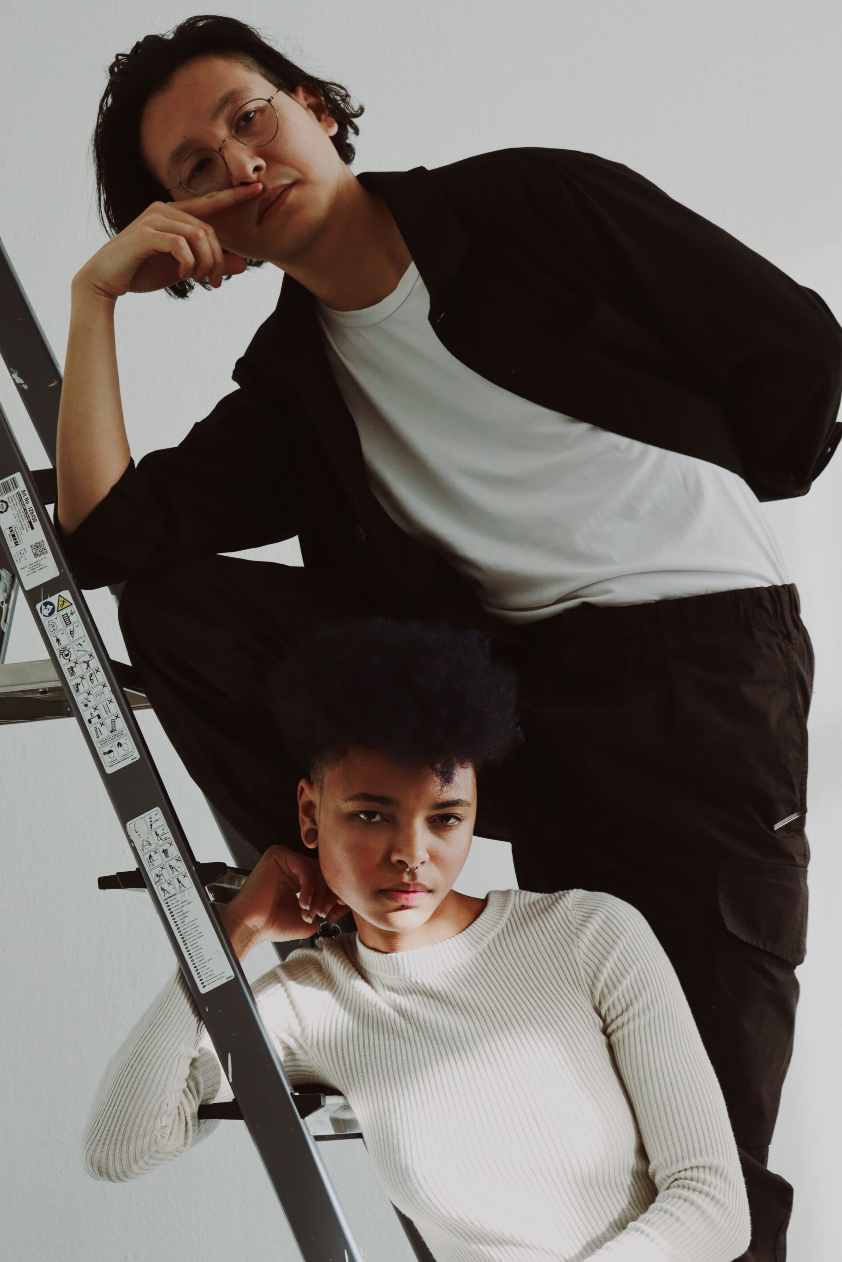 Contemporary studio shot of two models posing on a ladder with a minimalist white background.