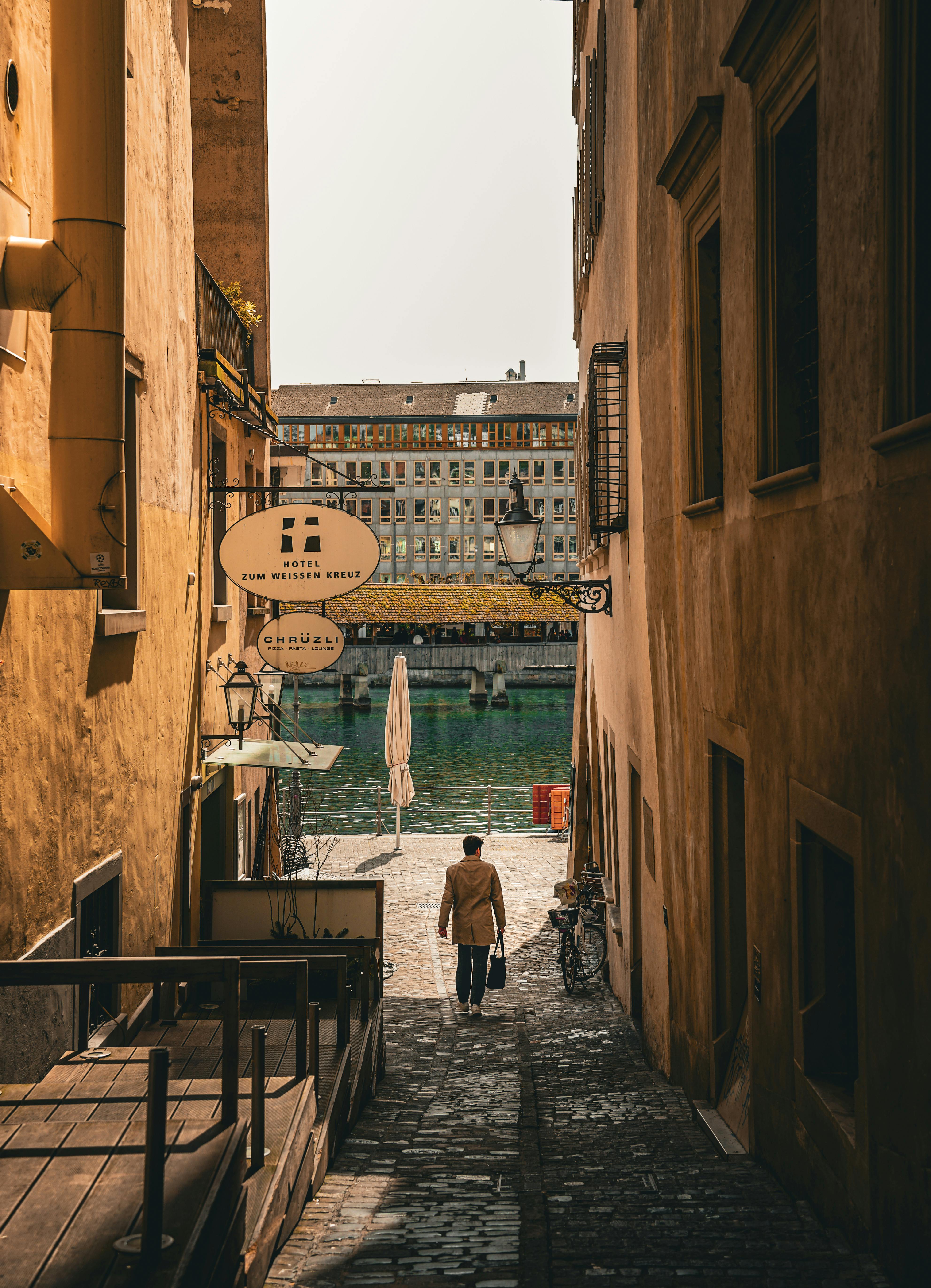 Idyllic scene of a man walking down a narrow alleyway in Lucerne, Switzerland, with cobblestone streets and sunlight.