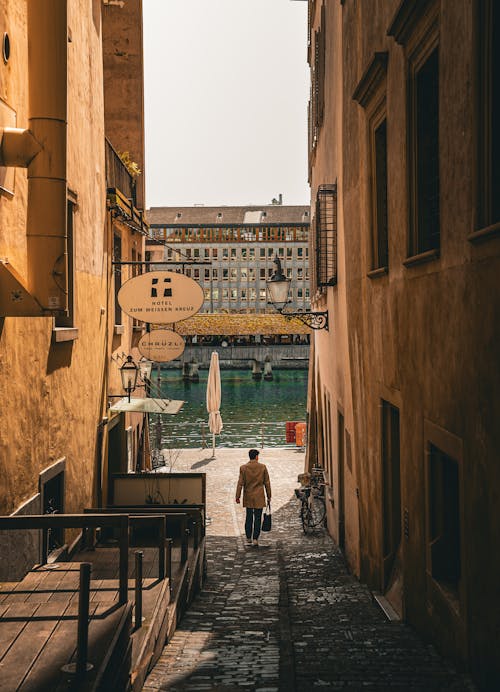 Back View of a Man Walking in an Alley between Buildings 