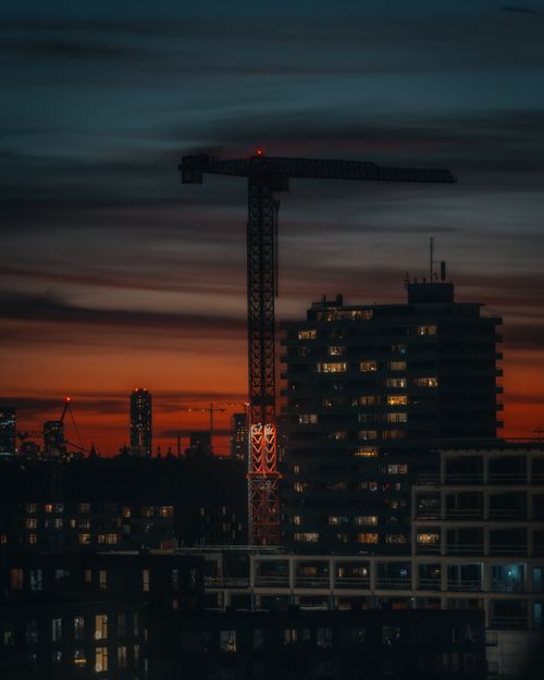 Free A striking view of a construction crane and urban skyline silhouetted against a vibrant sunset. Stock Photo