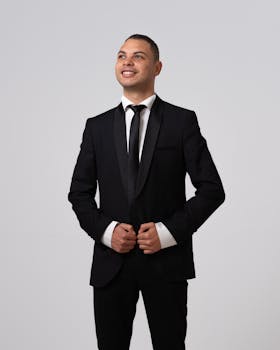 Stylish man in a black suit with a tie standing confidently against a white background.