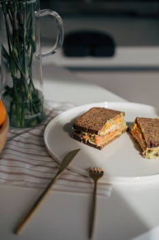 Tasty whole grain sandwich with salmon and greens on a white plate, perfect for lunch or a light meal.