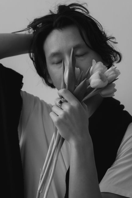 A monochrome portrait of a man with eyes closed holding flowers, exuding an artistic mood.