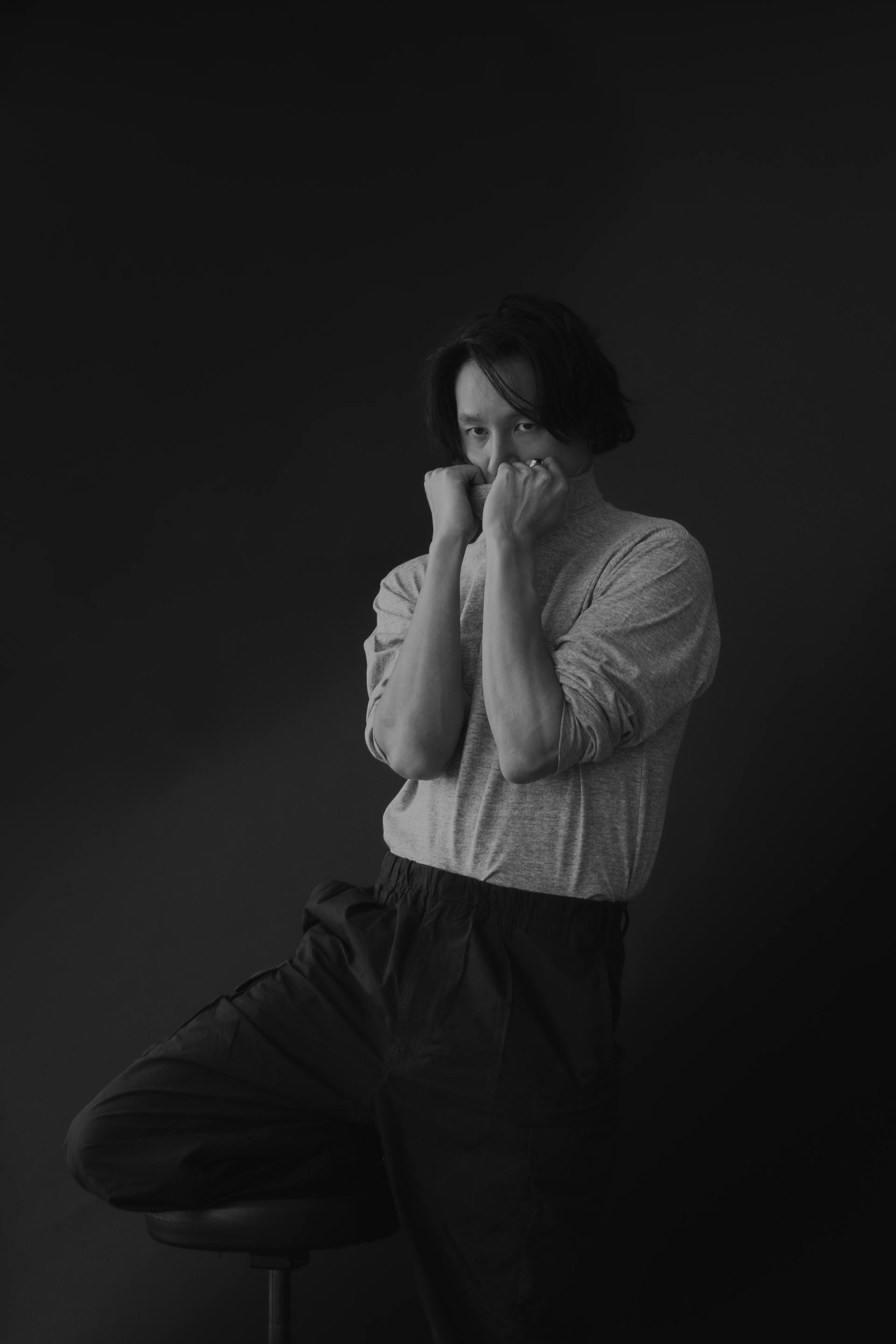 Studio portrait of a man in a relaxed pose with a dark background, wearing casual clothing.