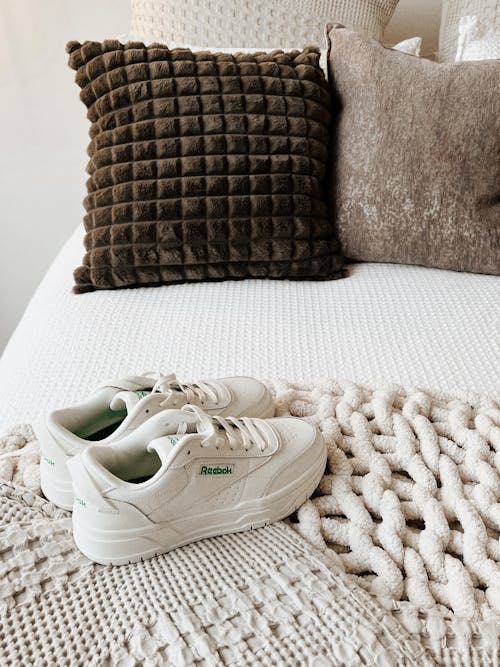 White Sneakers Standing on a Blanket on a Bed 