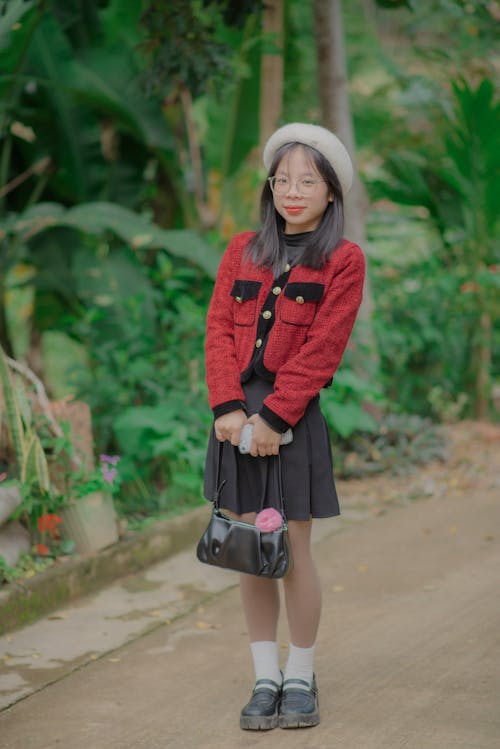 Model in a Red Jacket and Black Pleated Mini Skirt Holding a Handbag