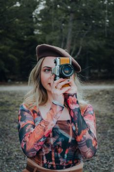 A fashionable woman with a vintage camera capturing nature outdoors.