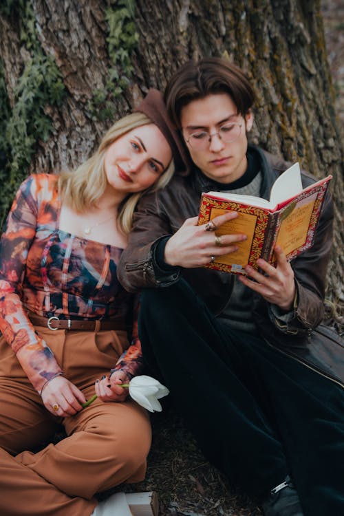 Free A Couple Sitting next to a Tree and Reading a Book  Stock Photo