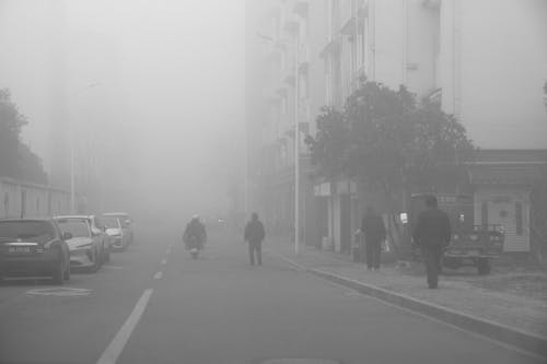A black and white photo of people walking down a street in the fog