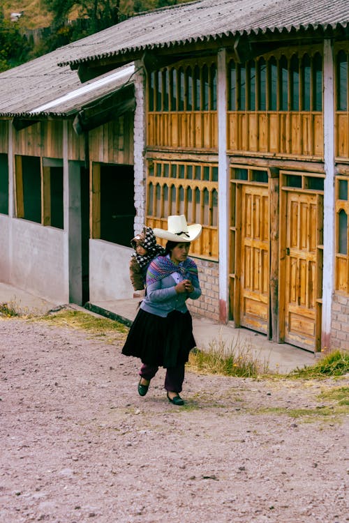 Mother in Hat Carrying Baby in Village