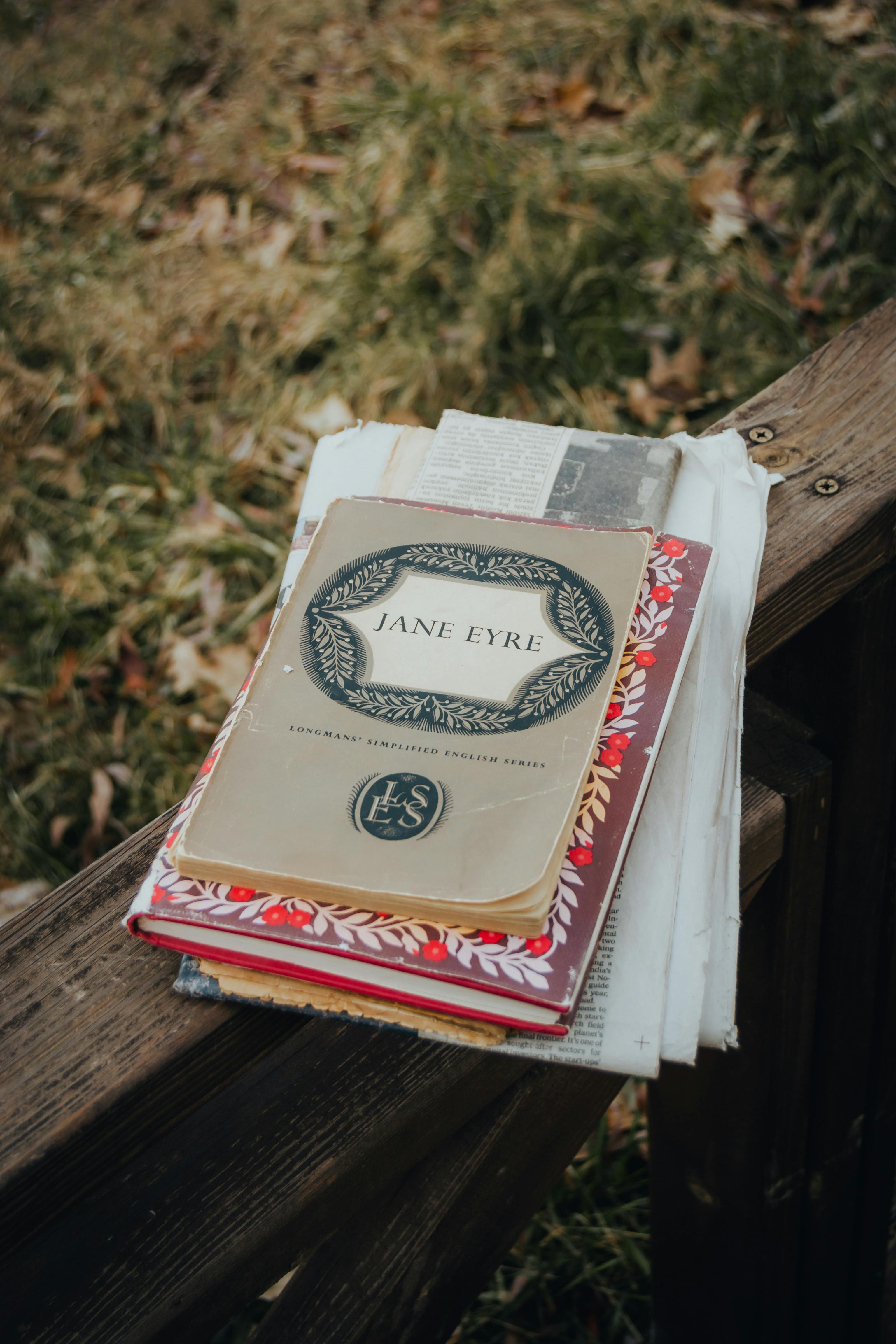A close-up of a vintage book stack including 'Jane Eyre' placed on a wooden fence outdoors.