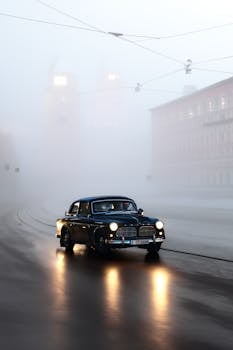 Classic Volvo car driving through foggy city street, creating a moody atmosphere.