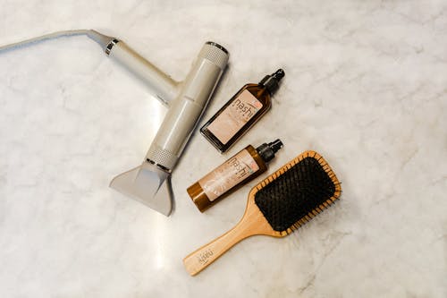 Hairbrush Hairdrier and Other Hair Products on Marble Table