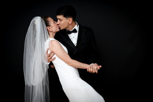 Newlyweds in Wedding Dress and Suit Kissing on Black Background