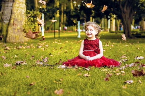 Girl in Red Dress Sitting on Grass at Park