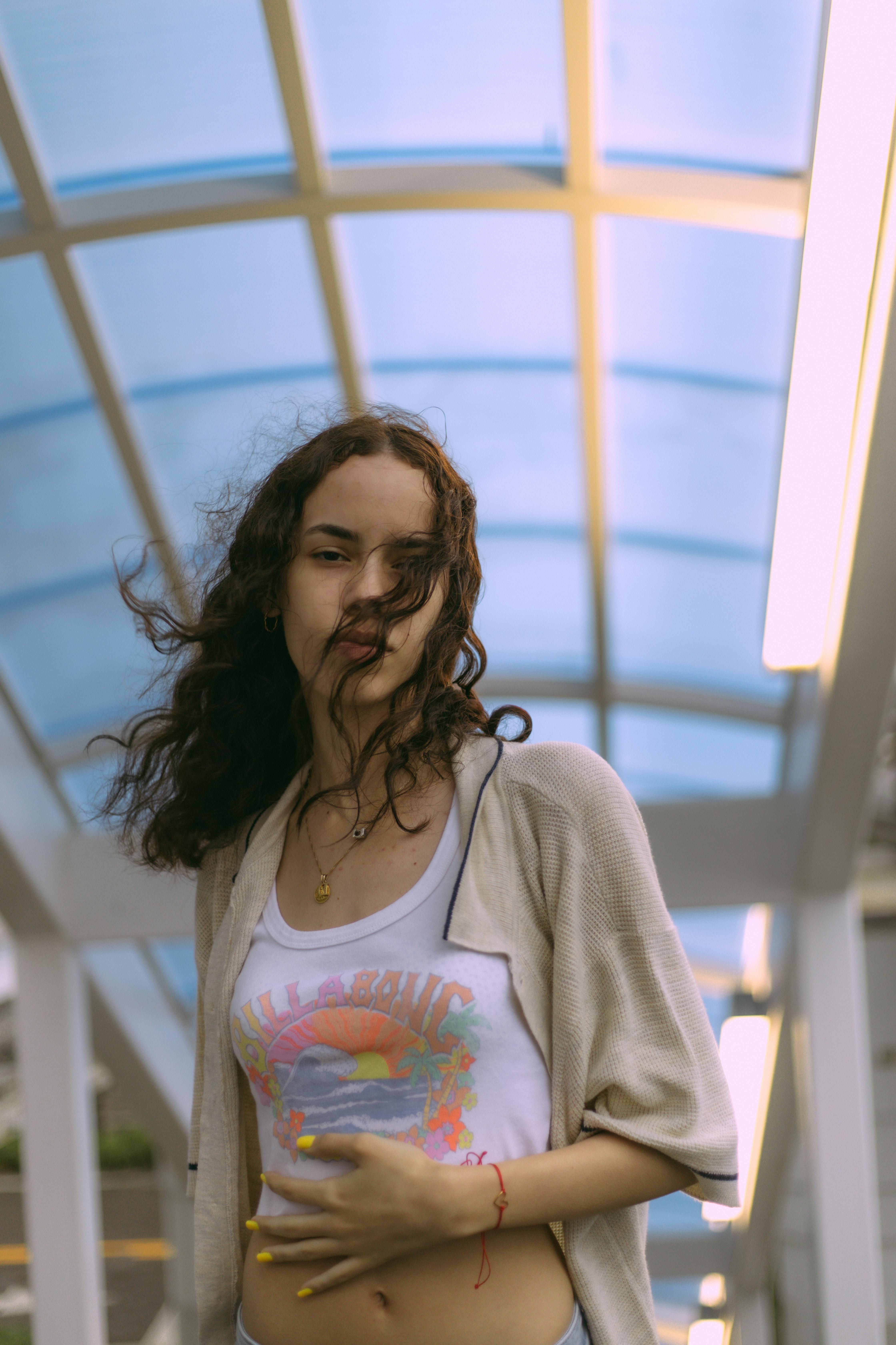 A young woman in a stylish casual outfit poses under a modern architectural structure.