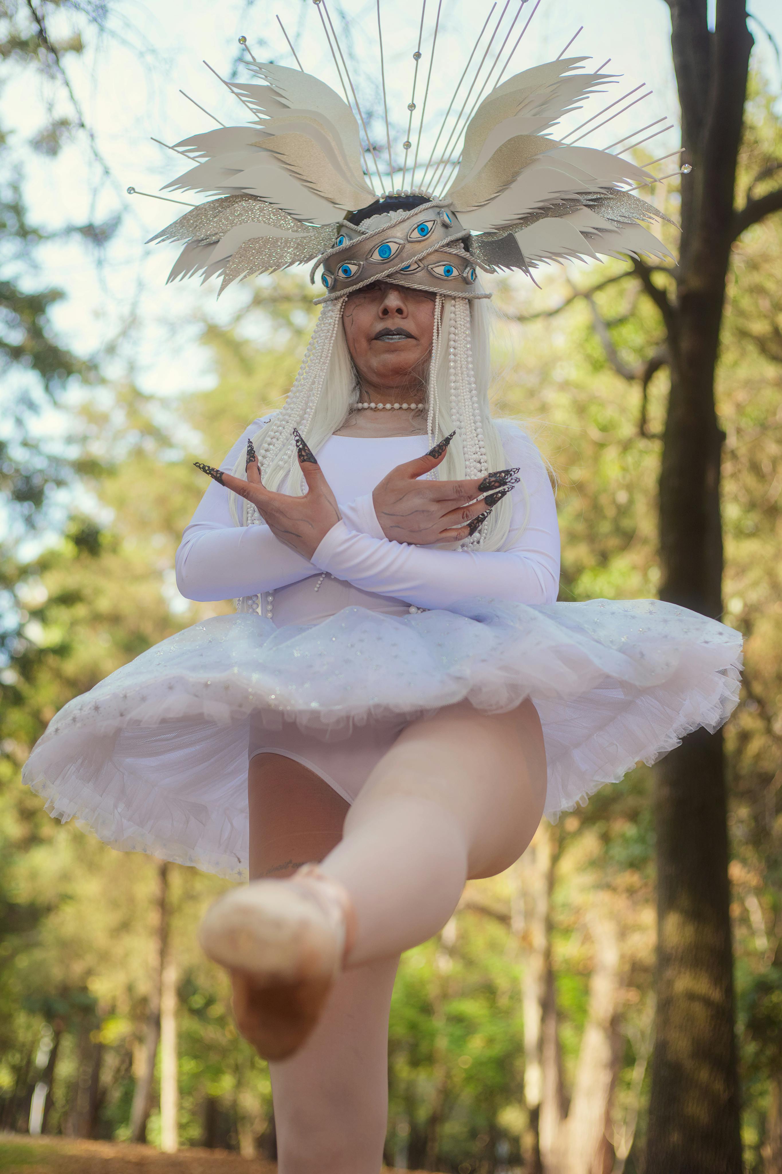 Free A performer in a white costume with feathers dances gracefully in an outdoor park setting. Stock Photo