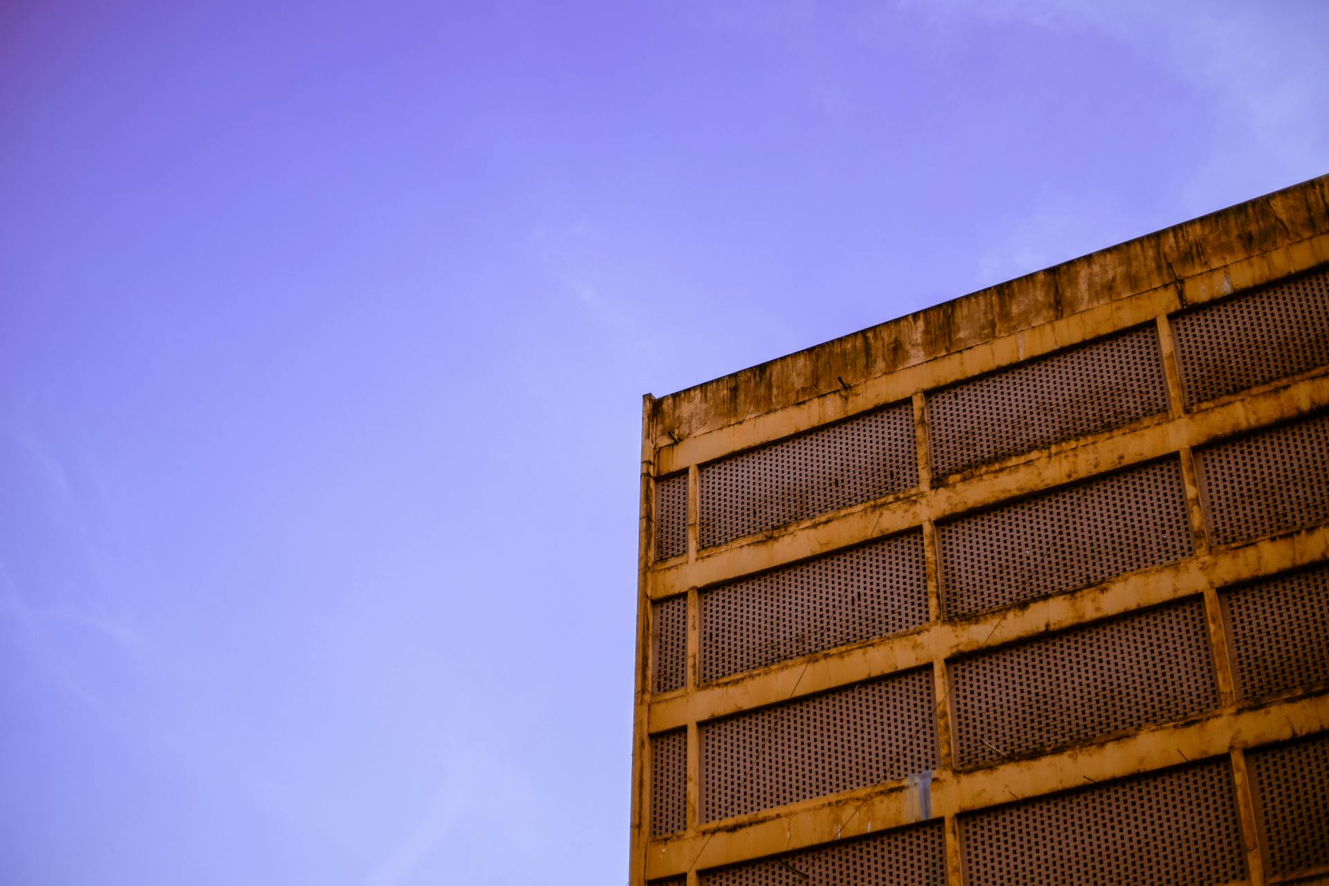 Vintage industrial facade with rust and mesh grates against a clear blue sky.