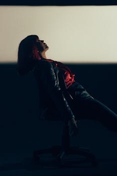 Woman with red hair and leather jacket striking a dramatic pose in studio lighting.
