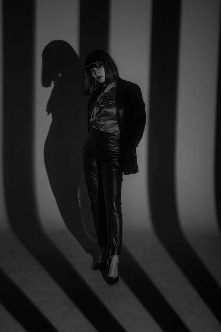 Artistic black and white photo of a woman posing stylishly with bold shadows in the background.