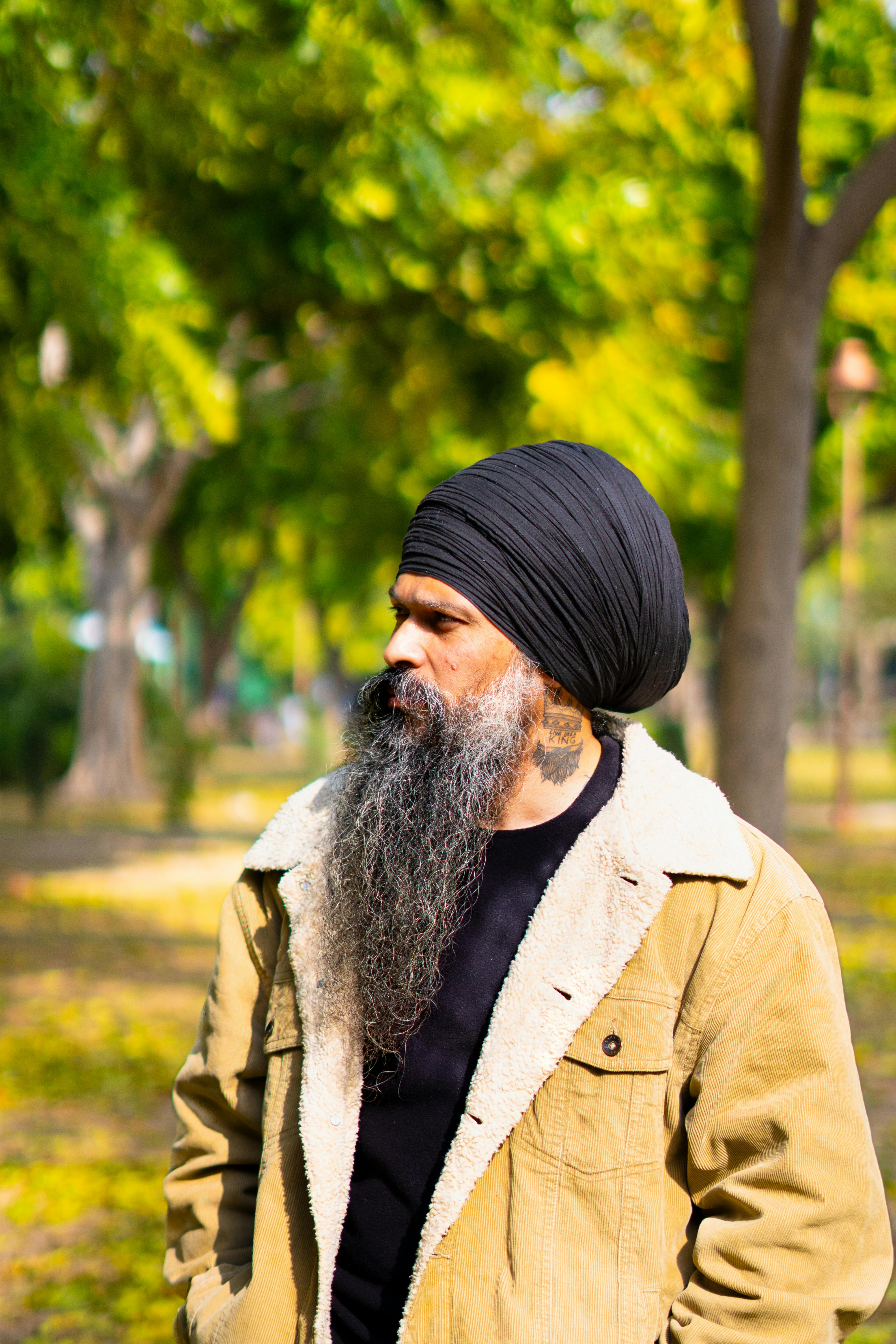 Portrait of a bearded man with a turban standing outdoors in a sunny park.