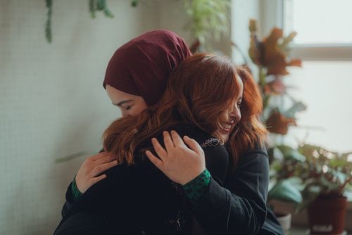Free Two women embracing warmly and smiling, surrounded by indoor plants, conveying friendship and affection. Stock Photo