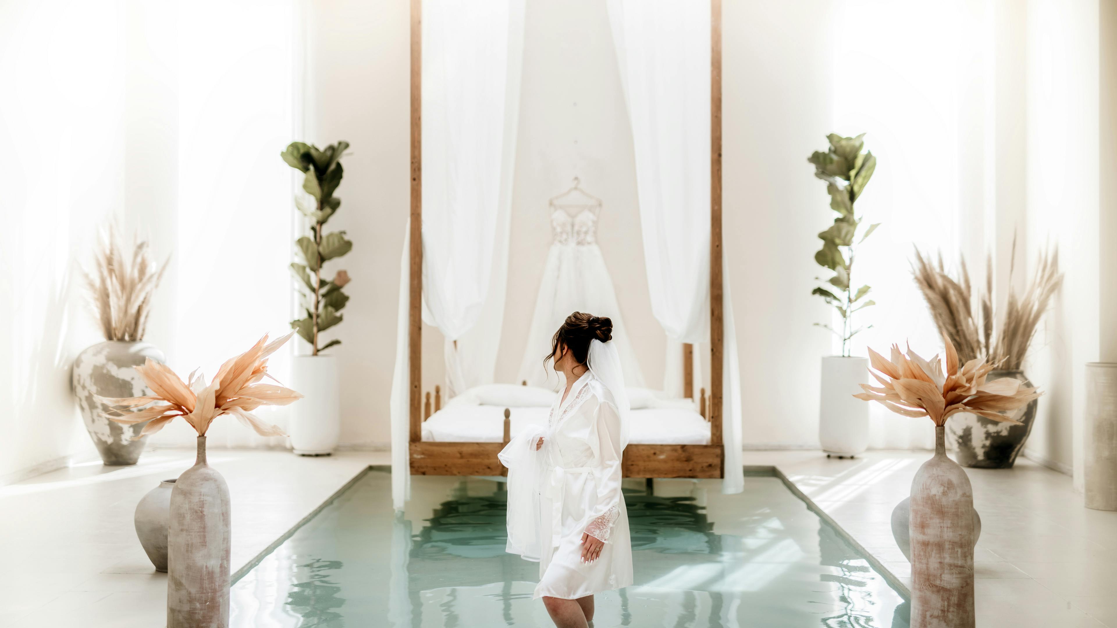 A serene bridal suite featuring a bride in a dressing gown, set against a luxurious interior with a canopy bed.