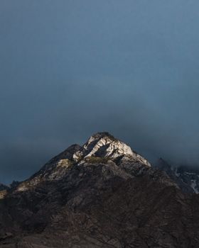 Capture of a solitary mountain peak illuminated by light with dark clouds above, Skardu, Pakistan.