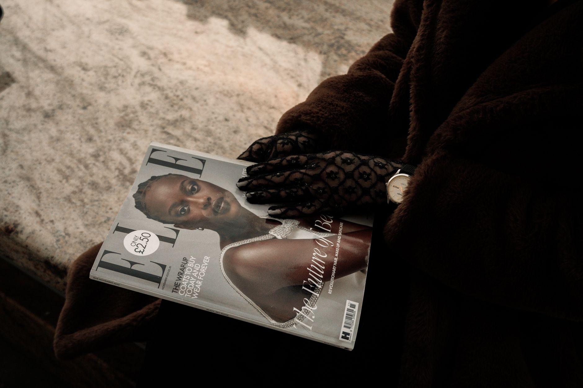 Stylish woman in brown coat holds a fashion magazine with gloved hands, showcasing elegance.