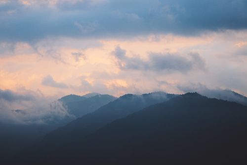 Free A serene view of a mountain range under a cloudy sky at dawn, capturing nature's tranquility. Stock Photo