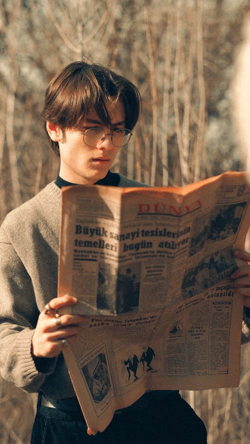 Young Man in a Gray Sweater Reading a Newspaper