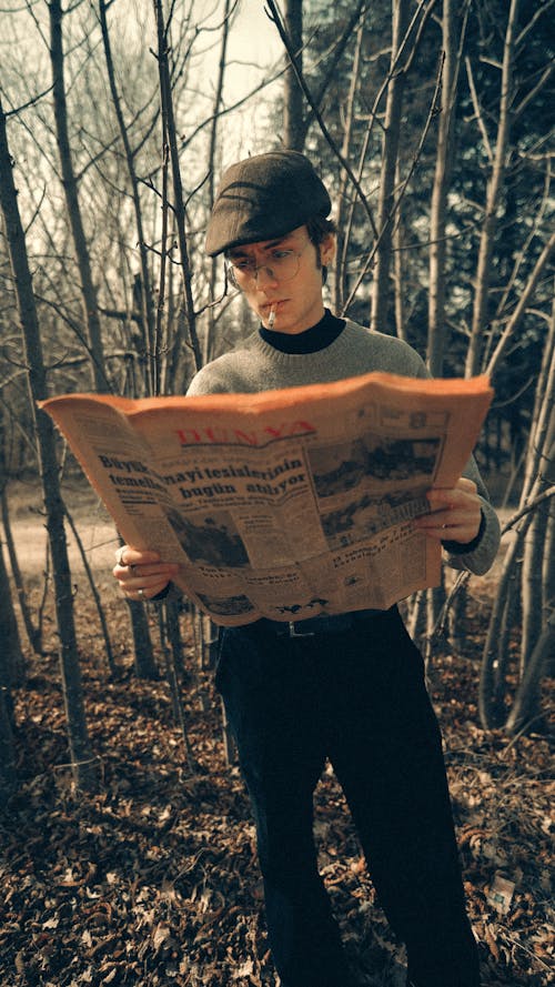 Young Man Reading a Newspaper and Smoking a Cigarette Standing in the Forest