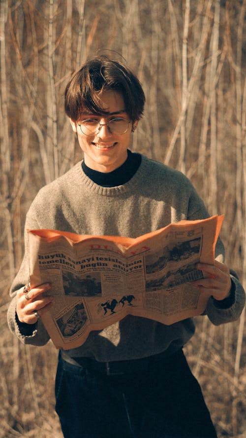 A young man holding a newspaper in the woods