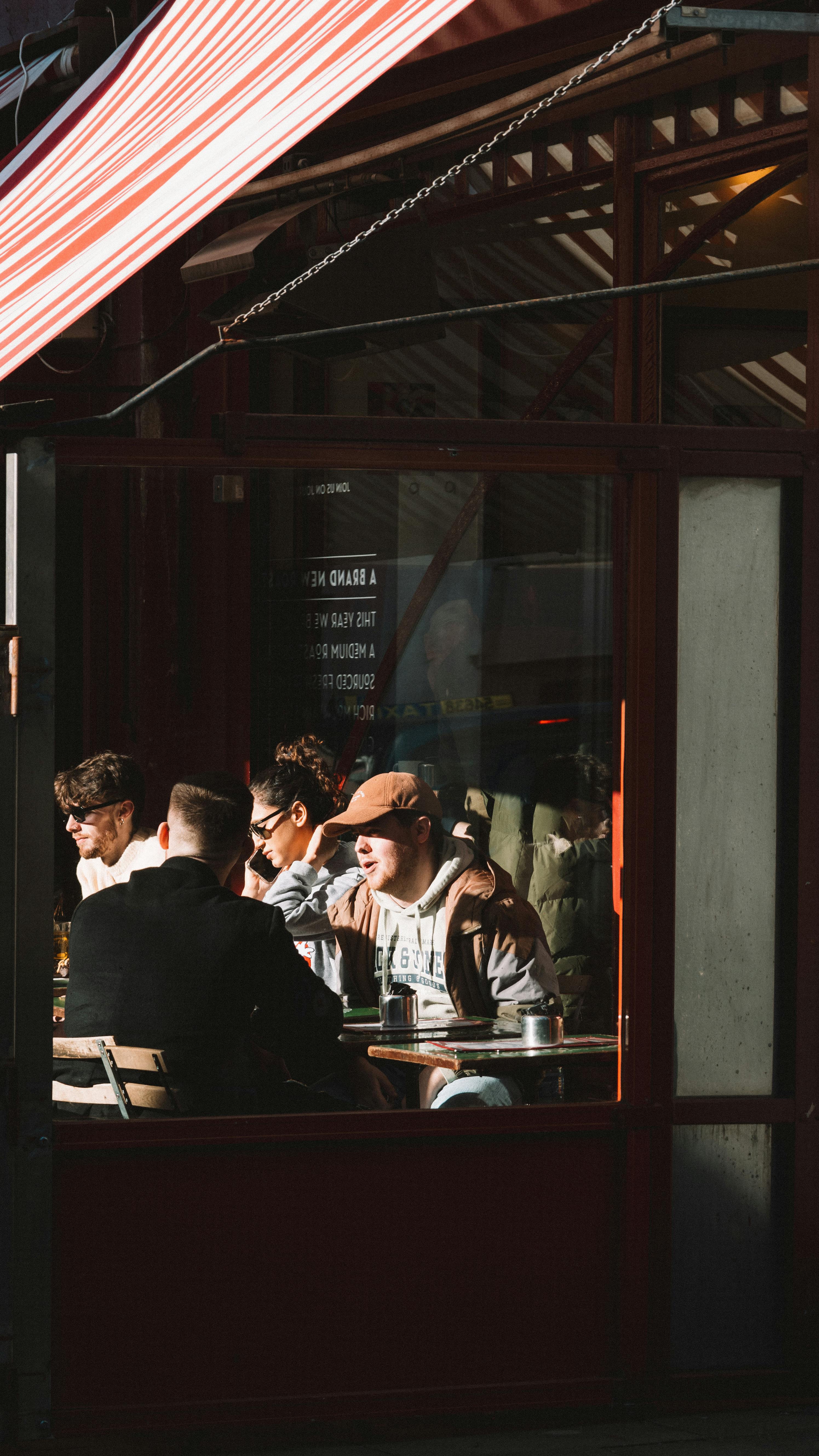 A group of adults enjoying conversation and relaxation at a sunlit café terrace.