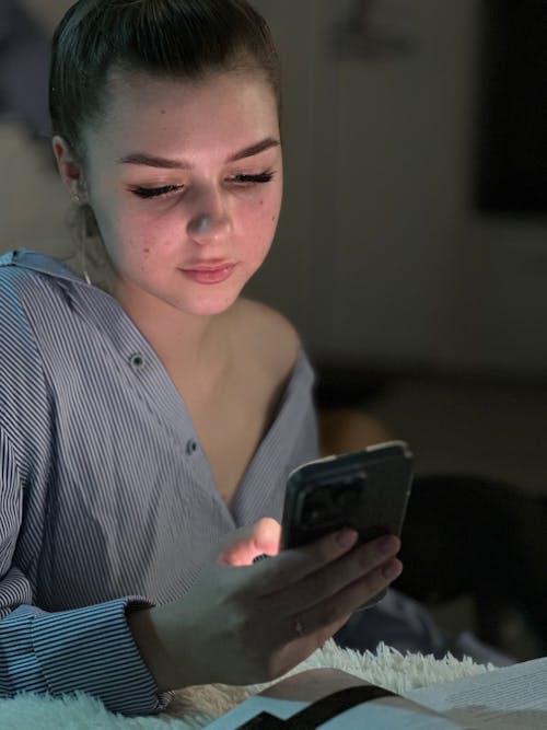 Young Woman Texting on a Smartphone over an Open Book