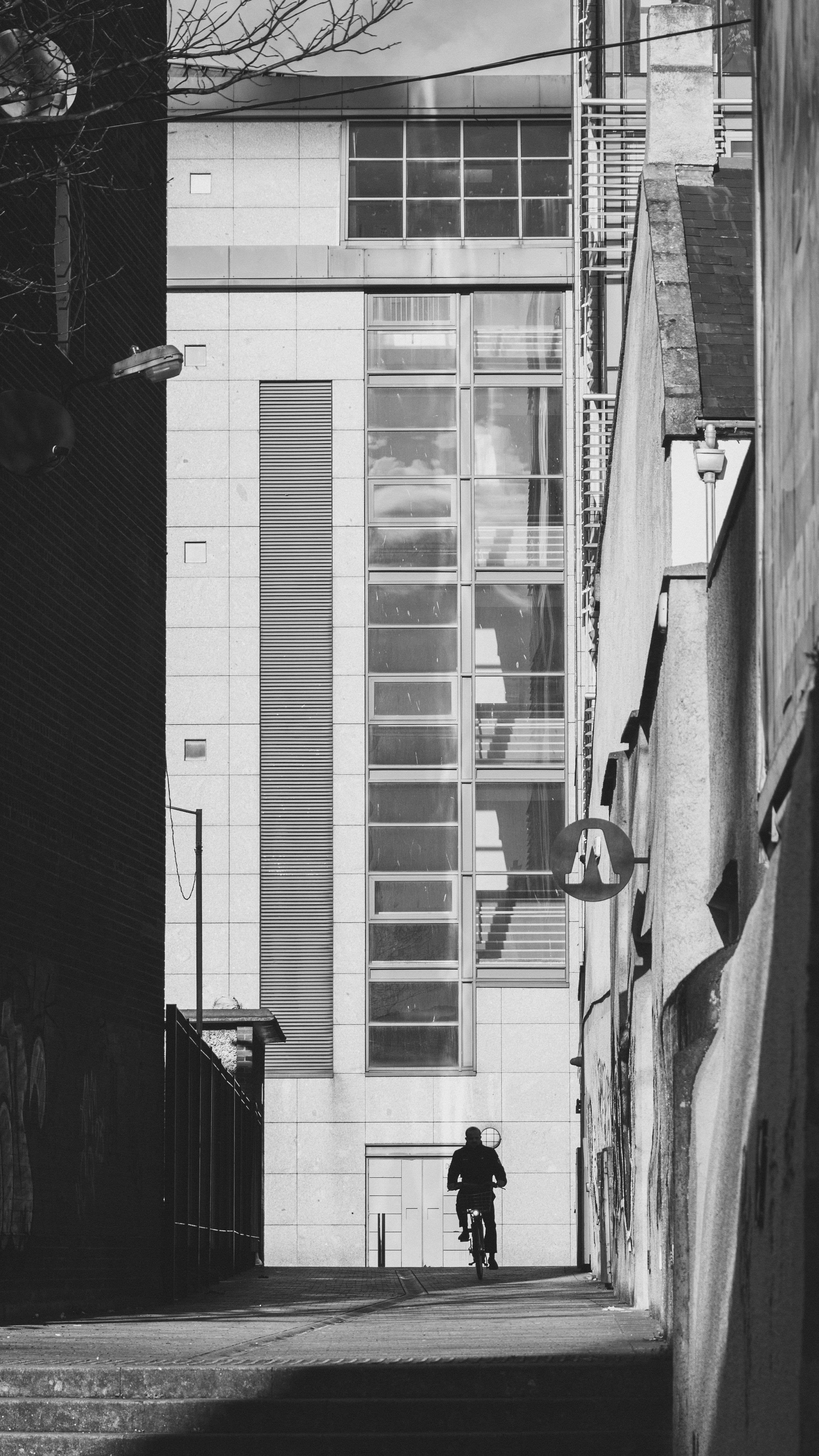 Silhouette of a cyclist in an urban alley with a modern building background.
