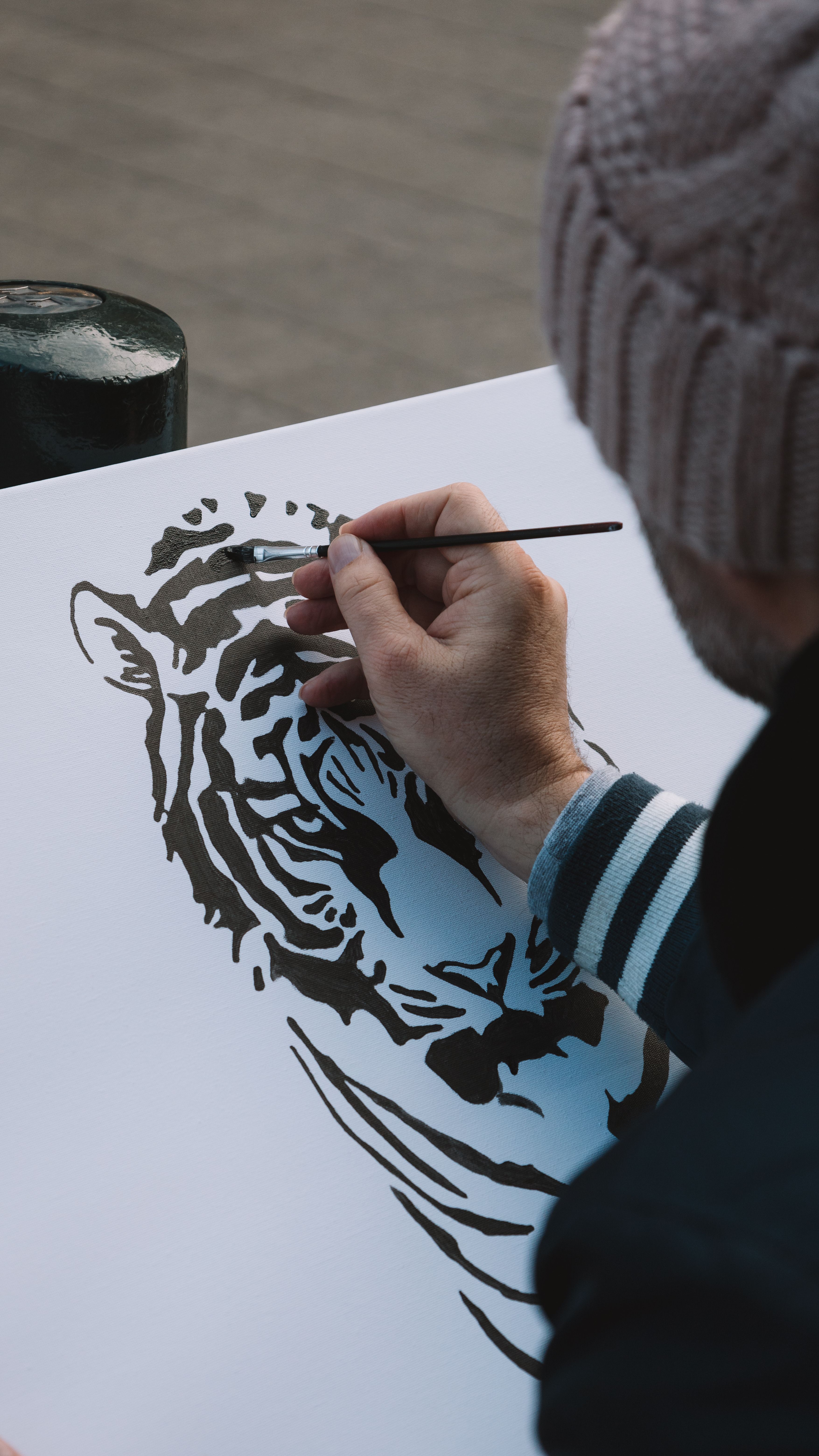 Man drawing a detailed tiger illustration on paper with a brush outdoors.
