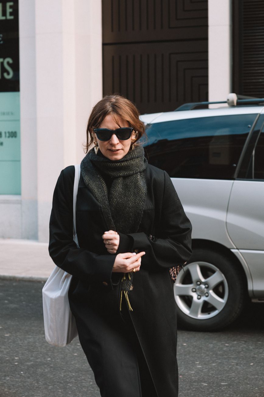 Fashionable woman in black coat and scarf walking in the city during winter day.