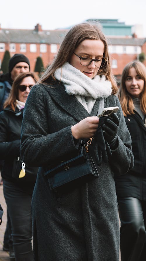 Woman in Coat and Eyeglasses Standing with Smartphone
