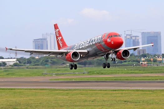 AirAsia aircraft landing on the runway at a bustling airport with city skyline in the background.