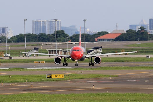 Red airplane taxiing on the runway with city skyline in the background.