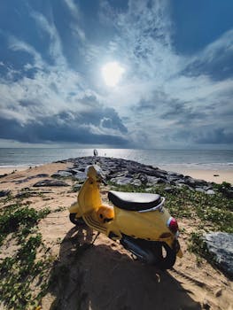 Vibrant yellow scooter parked on scenic Udupi beach with dramatic sky and sunlight reflecting on the sea.